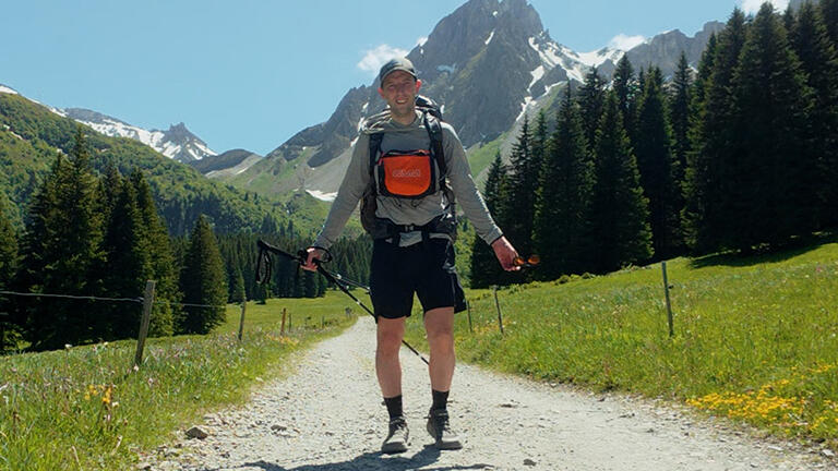 Peter M. Riley standing in hiking gear with mountains in the background.
